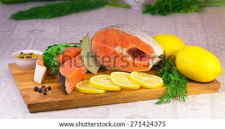 On the table are cut into large pieces of fish salmon, lemon, dill and parsley, spices for cooking fish.