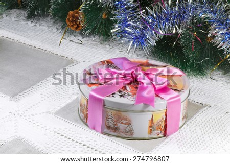 Beautiful box with a gift for Christmas, with the image of winter scenes, tied with a pink ribbon is Located near the decorated Christmas tree.