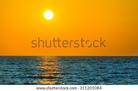 Seascape: the calm blue sea and the sun, leaning toward the horizon.