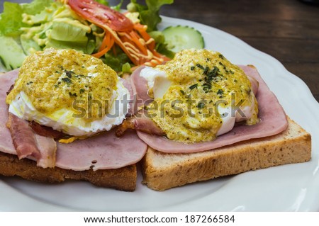 Two eggs benedict covered by curry powder on bacons, hams and toasts with salad on the white dish
