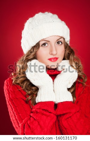 beautiful girl with curly hair wearing warm hat, mittens and red sweater over red background