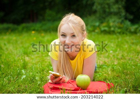 blonde smiling girl holding cell phone and listening music with white headphones