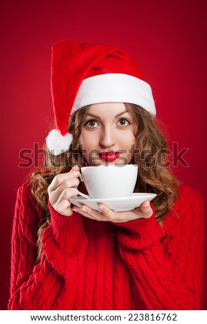 beautiful brunette girl in Santa Clause hat holding white mug  wearing red sweater  over red background