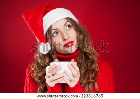 beautiful brunette girl in Santa Clause hat holding white mug  wearing red sweater  over red background