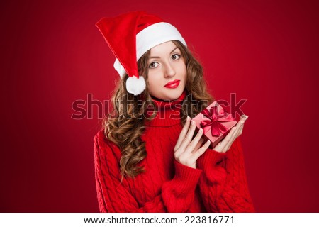 beautiful brunette girl in red sweater holding Christmas present wearing Santa Clause hat