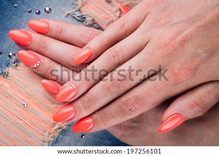 orange nails with cristals and hands on cloth background