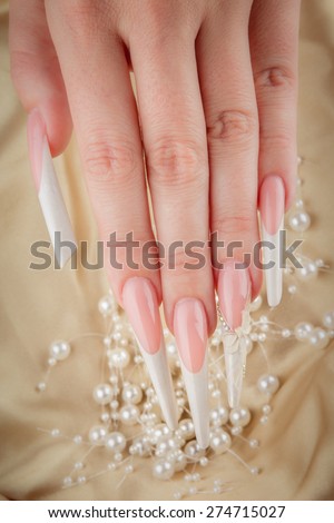 Painted extreme long nails and hands with pearl jewelry isolated on gold silk background