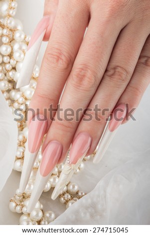 Painted extreme long nails and hands with pearl jewelry isolated on white silk background