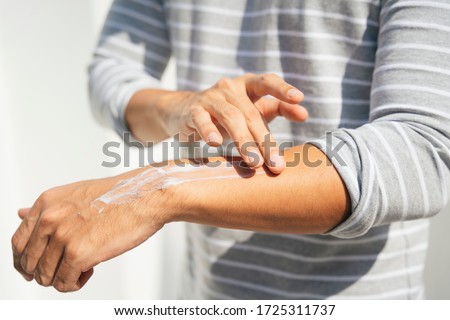 Hand of a man applying cream lotion on arms to protect the skin from UV sunlight. Solar protection. Sunblock lotion bottle. Sun Screen protection on man hand.