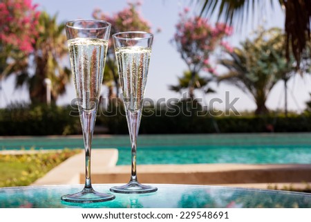 Two glasses of champagne on the glass table in outdoor resort bar