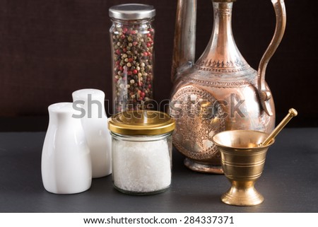 Concept of salt and pepper accessories. Mortar, jars with salt and pepper, old copper jar, porcelain salt and pepper on black stone background. Horizontal