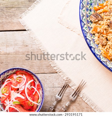 Pilaf and achichuk salad in handmade plate with antique forks on wooden background. Square, top view