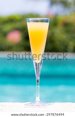 Glass of Bellini cocktail on the pool nosing at the tropical resort. Vertical
