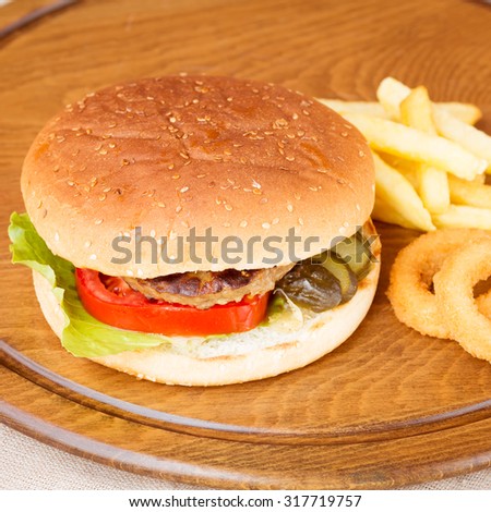 Classic homemade hamburger with onion rings and french fries on a wooden plate. Juicy homemade food. Square