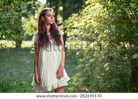 Beautiful young woman wearing elegant white dress standing in the forest
