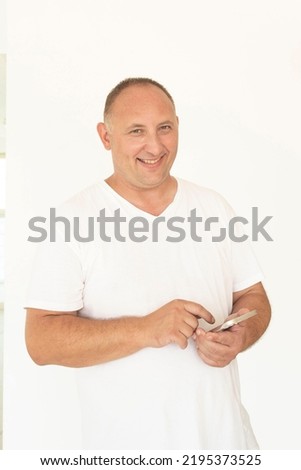 Cheerful guy, a man in a white T-shirt uses the phone.  Caucasian person smiling, texting, chatting.  The concept of online shopping, online dating, e-business, online store, smartphone. Foto stock © 