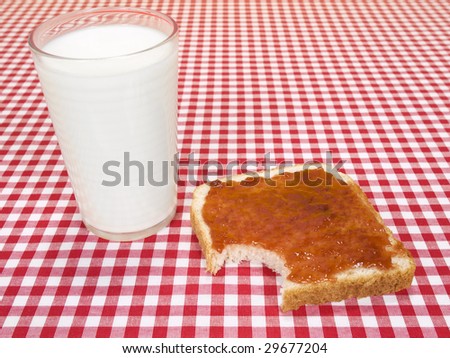A glass of milk and a toast spread with jam, with a bite missing.