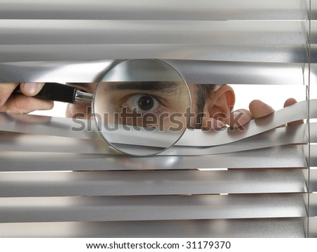 A man is peeping through the blinds with a magnifying glass.
