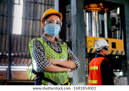 Factory woman worker or technician with hygienic mask stand with confident action with her co-worker engineer in workplace during concern about covid pandemic in people affect industrial business. Foto stock © 