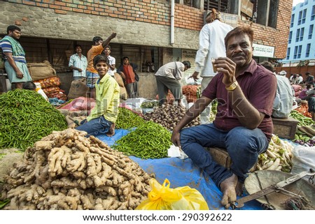 BANGALORE, INDIA - May 13, 2014: a man on break sips tea at his vegetable stall, other vendors in the background