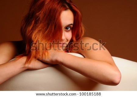A beautiful young red haired woman leaning over the back of a white chair