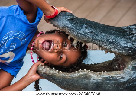 Alligator farm Miami Everglades girl puts head in crocodile mouth \
Funny female child puts head in mouth of fake alligator in tourist park Florida. For travel business blog websites book cover poster