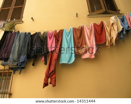 Lots of colorful clothes and towels hanging on a washing line in front of a tuscan house wall