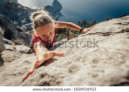Brave young woman climber fearlessly climbs up sheer stone wall in mountains, overcoming obstacles. Dangerous chasm balancing, adrenaline and courage in extreme sports. 商業照片 © 