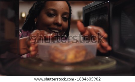 Afro-american woman using the microwave oven to heating food. View from inside microwave of african female heating up plastic container with buckwheat and chicken