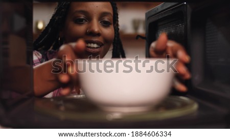 African woman reheat food in ceramic bowl using microwave oven. View inside microwave of meal in dish spinning and warming for afro-american female