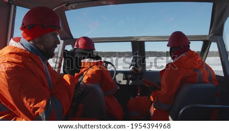 Professional lifesaving team sailing air-boat in arctic. Male rescuers in uniform crossing frozen river in hovercraft using portable radio and gps app on digital tablet Photo stock © 