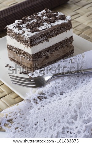 chocolate cake. mousse filled with chocolate and whipped cream on square plate and white flowers