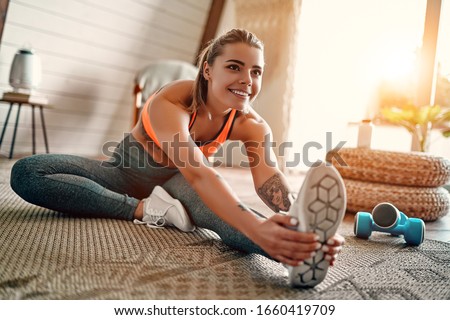 Athletic woman in sportswear doing fitness stretching exercises at home in the living room. Sport and recreation concept.
