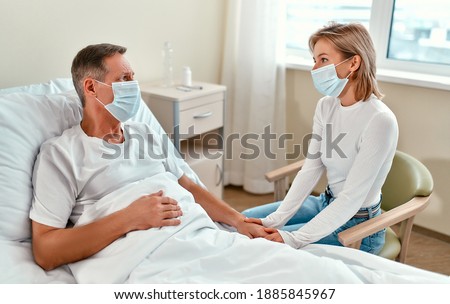 A beautiful girl in a protective medical mask came to visit her dad or grandfather, who is lying in a modern hospital ward during the coronavirus or covid-19 epidemic. Foto stock © 