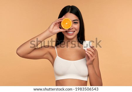 Portrait of Asian young girl holding orange and moisturizing face cream isolated on beige background. Facial skin care concept, natural cosmetics. Foto stock © 