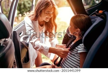 A cute woman mother put her daughter in a car seat and fastens her seat belts. Protection during the trip in the car. Stock foto © 