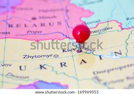 Round red thumb tack pinched through city of Kiev on Ukraine map. Part of collection covering all major capitals of Europe.
