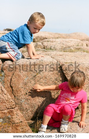 Young girl and young boy climbing down a large rock in sunny weather.
