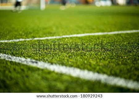 Close-up of artificial turf. Blurred legs of soccer players in the background.