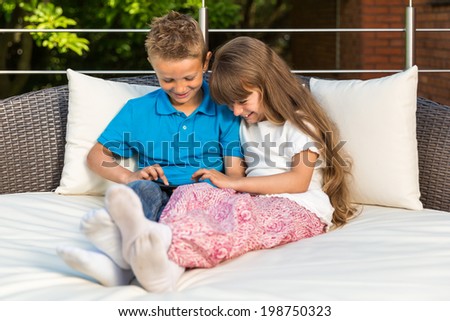 Boy and girl sitting on patio and having fun with their tablet.