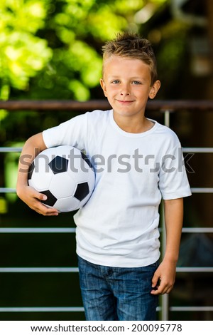 Caucasian boy holding his soccer ball under his right arm.