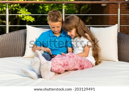 Boy and girl sitting on patio and having fun with their tablet.
