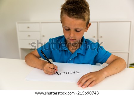 Young caucasian boy writing letters on a white piece of paper.