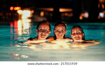 Tanned caucasian kids in a resort swimming pool during night time.