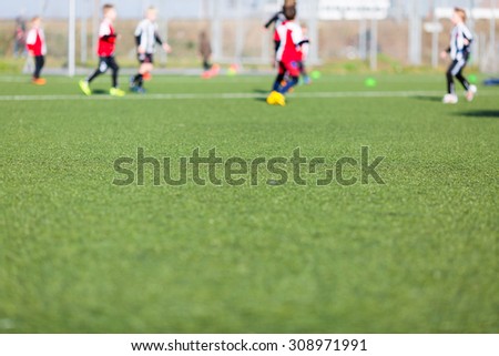 Blur of young kids playing a soccer training match outdoors on an artificial soccer pitch.