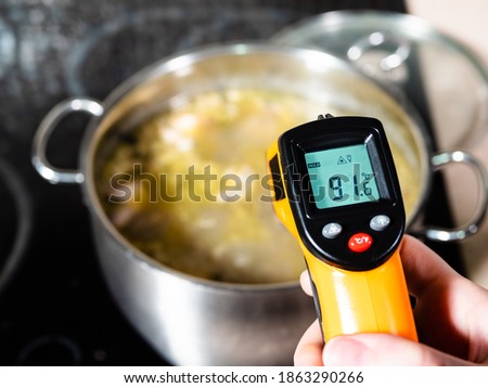 measuring temperature of fish soup during cooking in stockpot by infrared thermometer on ceramic stove at home kitchen ストックフォト © 