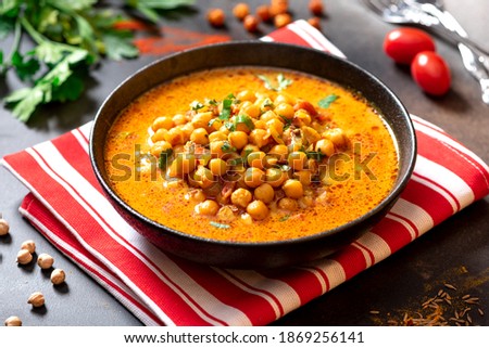 Hot spicy soup with chickpeas, onions, and tomato in a black ceramic bowl on a dark background close-up. Tasty vegetarian food, Indian dish.