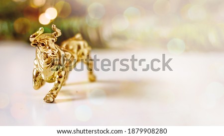 Golden calf, golden bull.Chinese new year of the bull. Year of the bull according to the Chinese calendar 2021. Souvenir bull made of gold metal on a background of fir branches with bokeh effect