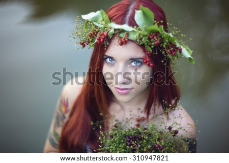 Bright girl with red hair. With a bouquet of berries and leaves on his head. The girl with a tattoo nature.
