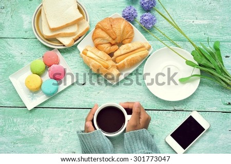 Female hands holding cups of coffee on vintage wood table with breakfast.